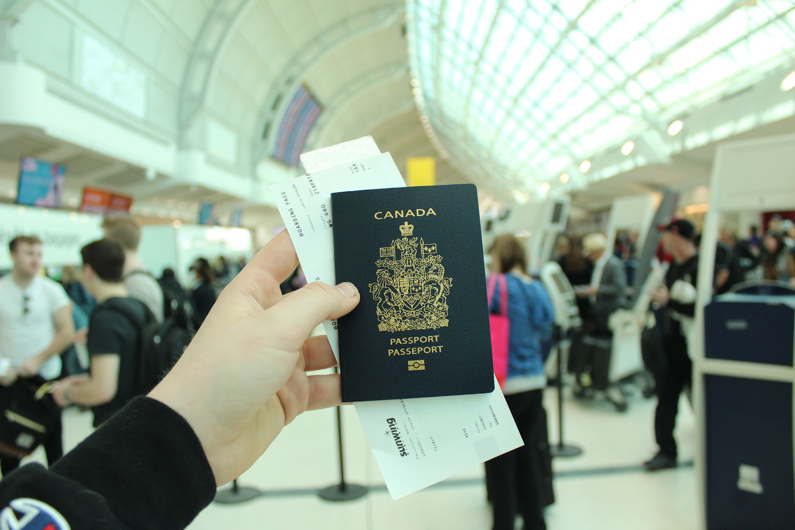 A person holding a Canadian passport and boarding passes at an airport terminal, preparing for international travel.