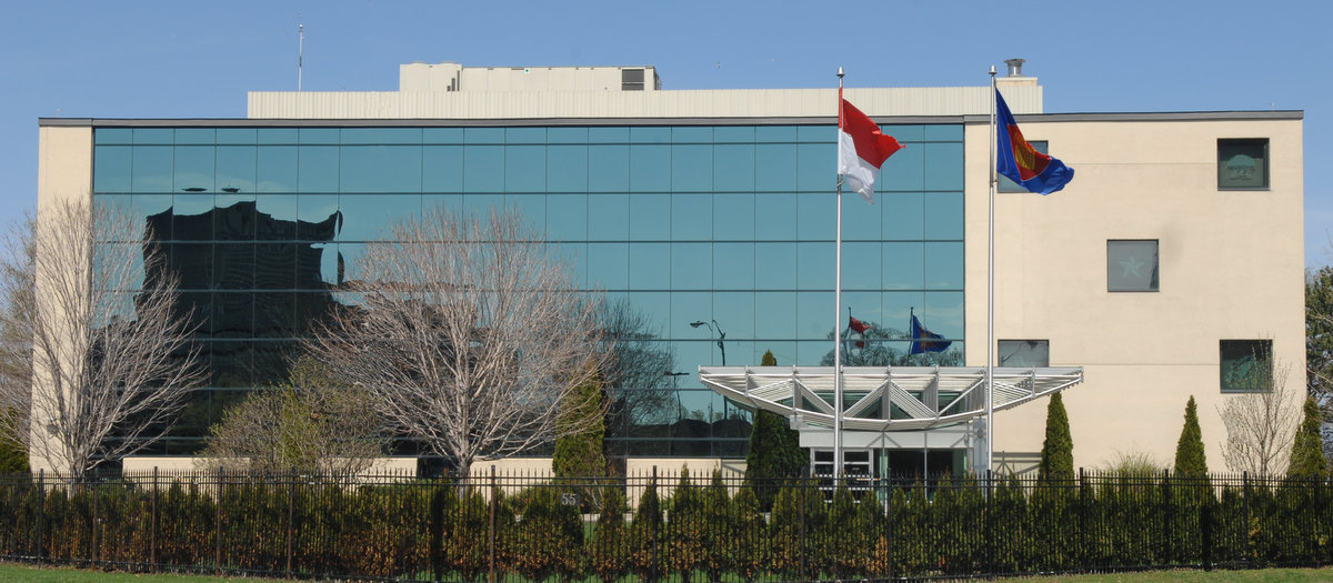 The Embassy of the Republic of Indonesia in Ottawa, Canada. The modern building features large reflective windows, with Indonesian and ASEAN flags displayed prominently at the front.